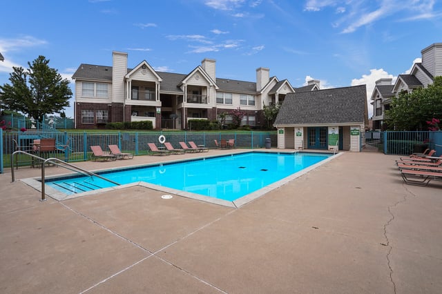Outdoor swimming pool with lounge chairs and apartment buildings in the background.