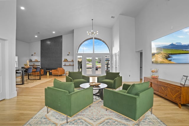 Modern lounge area with green chairs and a coffee table, facing large arched windows.