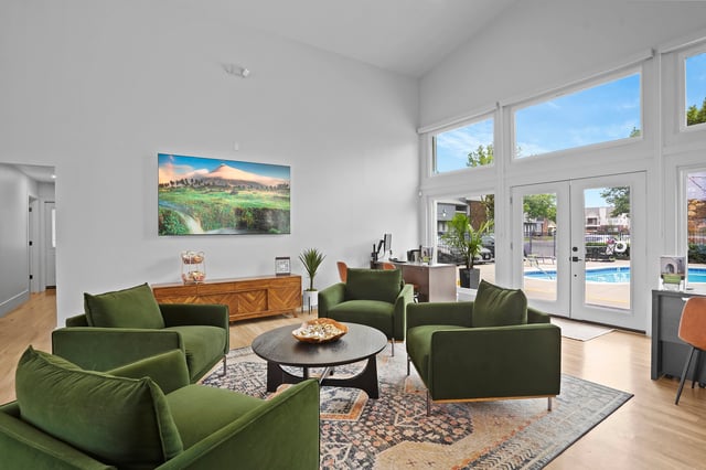 Lobby area with green chairs, coffee table, and artwork, overlooking a pool.