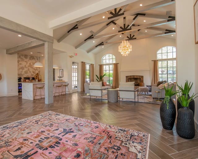 A large, open-concept living room with a patterned rug on the floor and a chandelier hanging from the ceiling.
