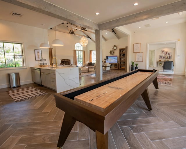 A pool table is in the middle of a room with a kitchen in the background.