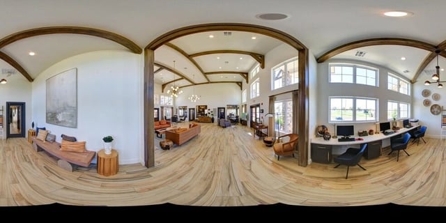 Spacious community lounge area with seating, desks with computers, and large windows.