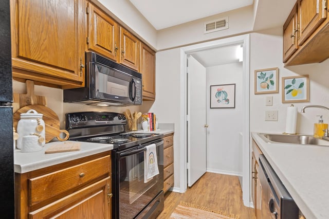 Kitchen with wooden cabinets, black appliances, and a doorway to another room.