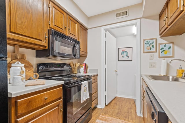 Kitchen with wooden cabinets, black appliances, and a doorway to another room.