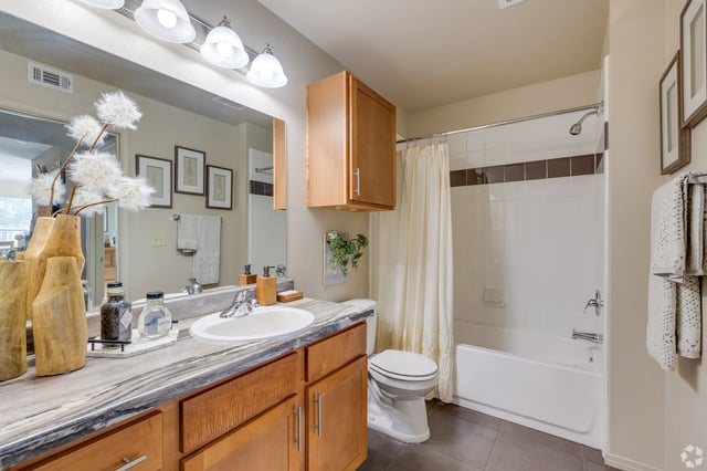 Bathroom in an apartment with a wooden vanity, large mirror, and a shower-tub combo.