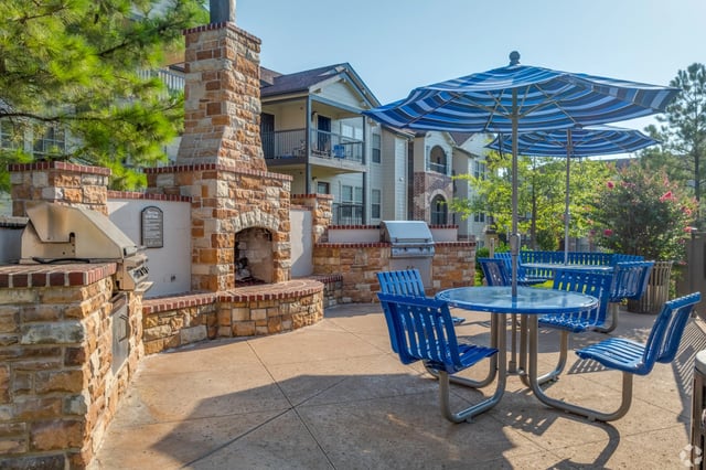 Outdoor communal grilling area with a stone barbecue, seating, and blue striped umbrellas.