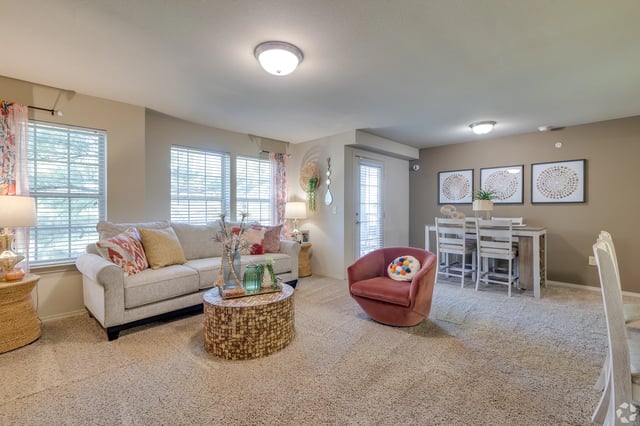 Bright apartment living room with neutral tones, gray sofa, pink chair, and dining area.