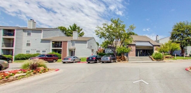 Exterior view of apartment buildings with parking lot and landscaping.