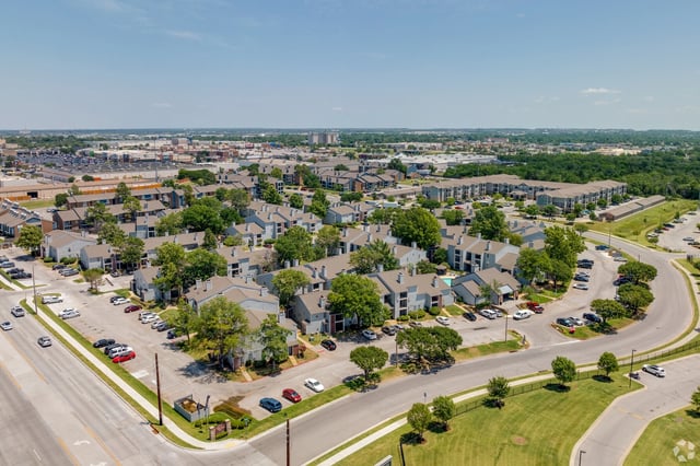 Aerial view of a multifamily property with multiple buildings, parking lots, and landscaping.