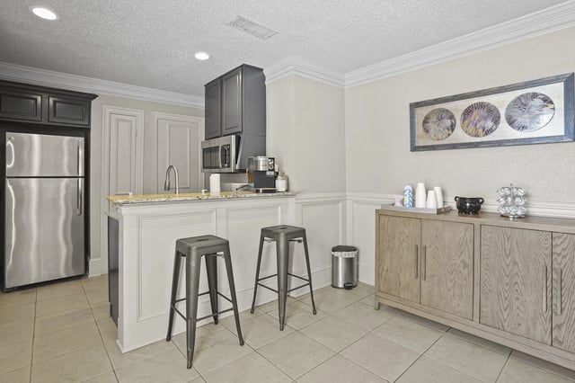 A kitchen with a refrigerator, bar stools, and a cabinet.