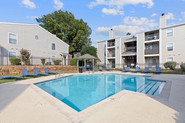 Sparkling swimming pool with lounge chairs and a gazebo at an apartment complex.