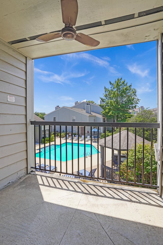 View of a sparkling swimming pool from a private balcony with a ceiling fan.