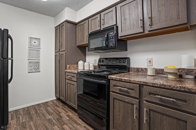 Modern kitchen with dark wood cabinets, black appliances, and granite countertops.