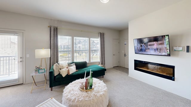 Living room with a green chaise sofa, a white ottoman coffee table, and a wall-mounted TV above a fireplace.