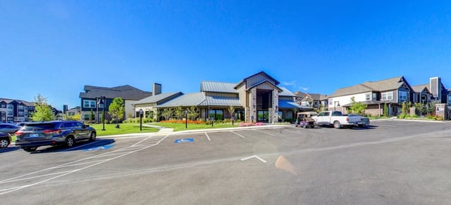 Exterior of apartment buildings with a parking lot and a clubhouse.