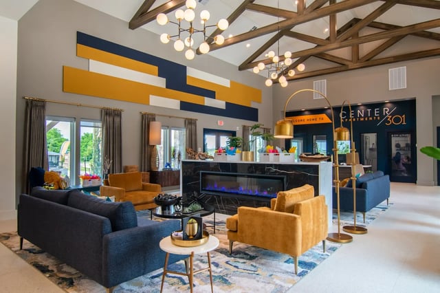 Modern apartment community lobby with blue-yellow geometric wall art, seating, and a marble fireplace.