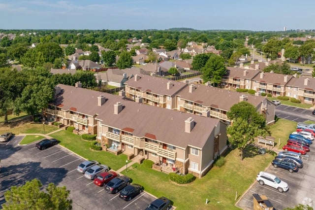 Exterior aerial view of apartment buildings with parking lot and surrounding neighborhood.