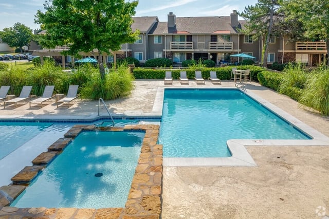 Outdoor swimming pool and hot tub area with lounge chairs and apartment buildings in the background.