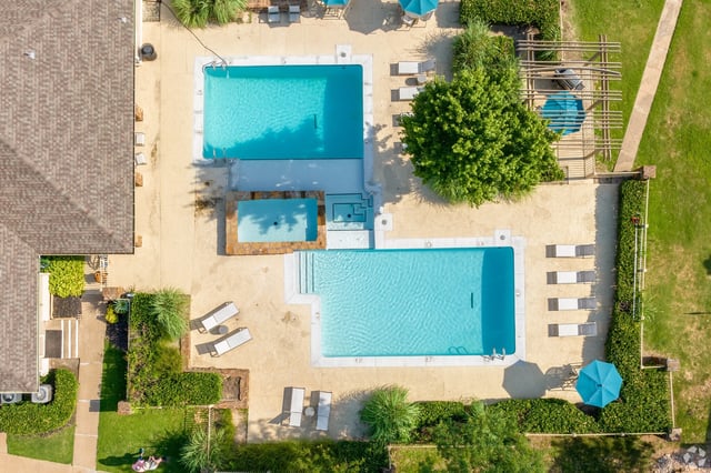 Aerial view of a swimming pool and hot tub area with lounge chairs and umbrellas.