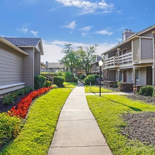 Sidewalk leading through a well-maintained courtyard with manicured lawns, flower beds, and apartment buildings.