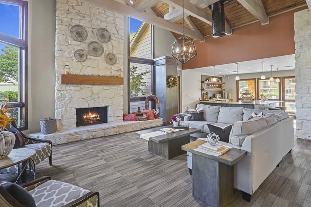 Open-concept community lounge with a large stone fireplace, vaulted beams, and a modern open kitchen.
