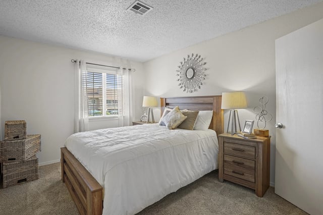 Bedroom in an apartment with a wooden bed, two nightstands, lamps, and a window.
