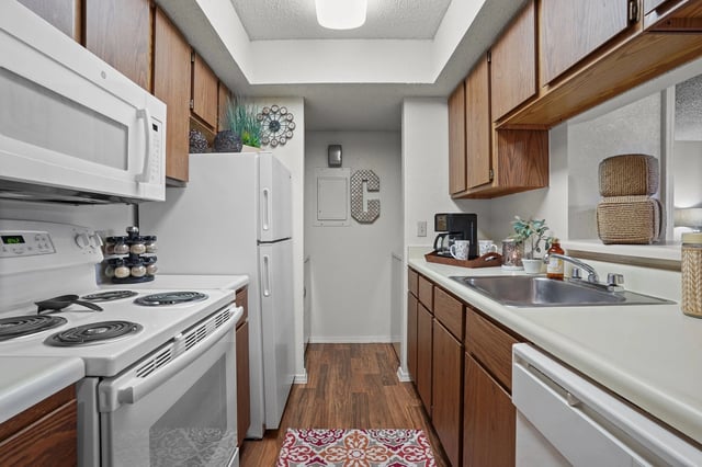 Narrow galley kitchen with white appliances, wood cabinets, and a double sink.