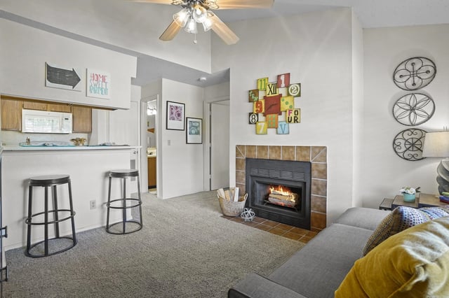 Living room with fireplace, sofa, and a kitchen pass-through with two bar stools.