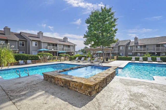 Outdoor community pool area with a stone spa, lounge chairs, and umbrellas.