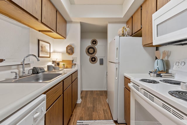 Kitchen with wood cabinets, white countertops, stainless steel sink, and white appliances including a stove and refrigerator.