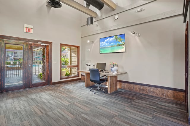 Reception desk with computer and printer, view of pool area through glass doors.