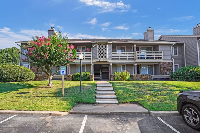Exterior view of apartment building entrance with lush landscaping and reserved parking sign.