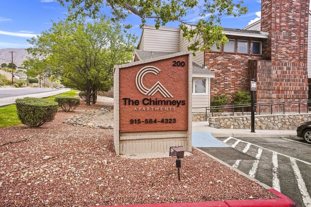 Exterior sign for The Chimneys Apartments with brick building and landscaping.