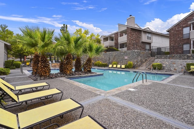 Outdoor apartment community pool with lounge chairs and palm trees.