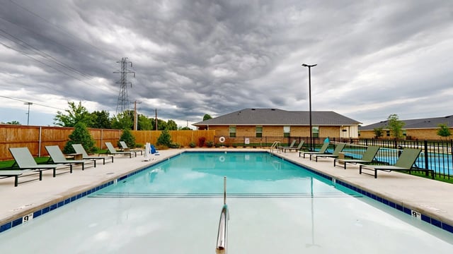 Outdoor swimming pool with lounge chairs and cloudy skies.