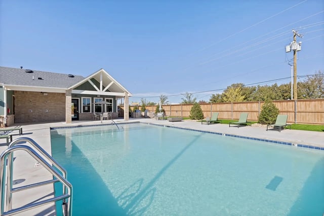 Swimming pool with lounge chairs and a building with covered seating.