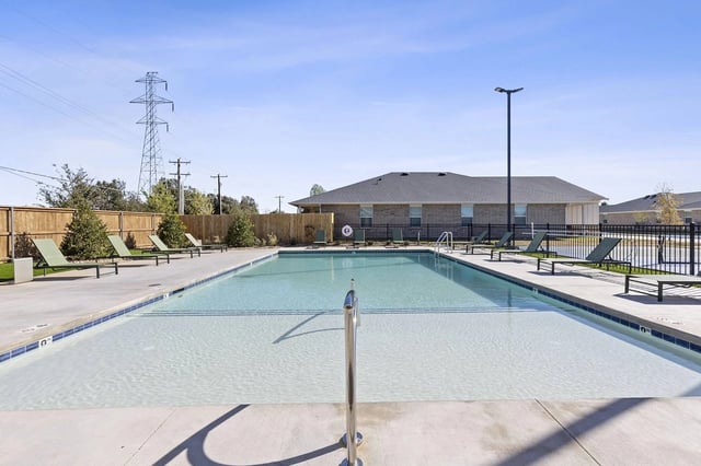 Outdoor swimming pool with lounge chairs and buildings in the background.