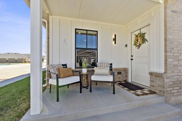 Porch with two chairs and a small table in front of a white door with a wreath.