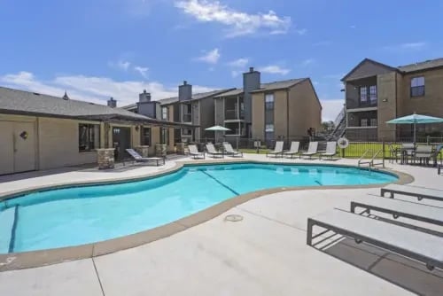 Resort-style swimming pool with lounge chairs and surrounding apartment buildings.
