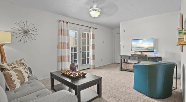 Living room with gray sofa, teal armchair, coffee table, TV, and ceiling fan.