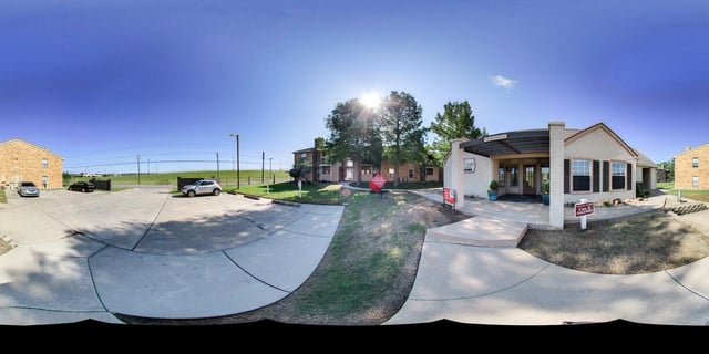 Exterior view of apartment buildings and leasing office with cars in the parking lot on a sunny day.