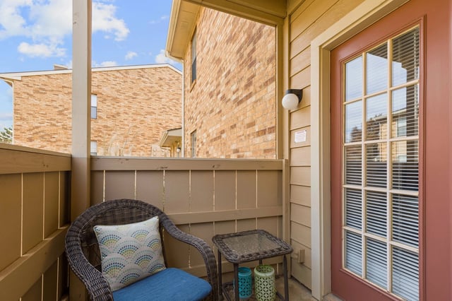 Balcony with a wicker chair and table overlooking brick buildings.