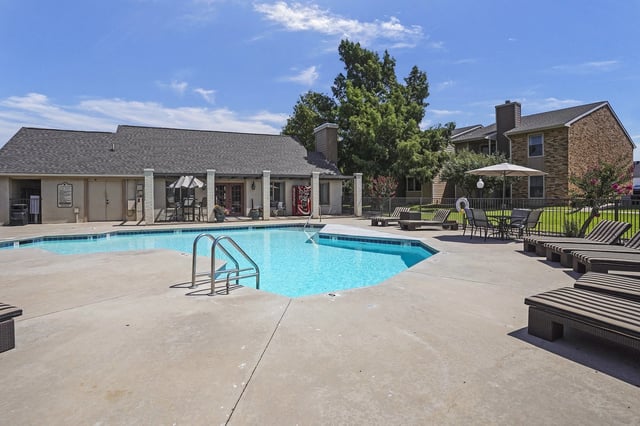 Resort-style swimming pool with lounge chairs and umbrellas, adjacent to apartment buildings.