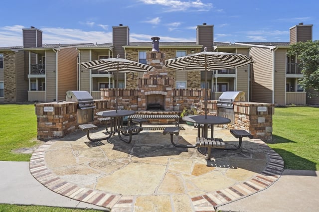 Outdoor grilling and dining area with built-in grills, fireplace, picnic tables, and umbrellas.