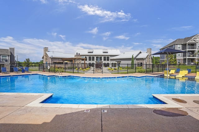 Outdoor swimming pool and lounge area with apartment buildings in the background.