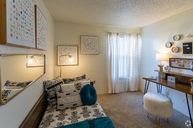A bedroom with a twin bed, desk, and artwork.