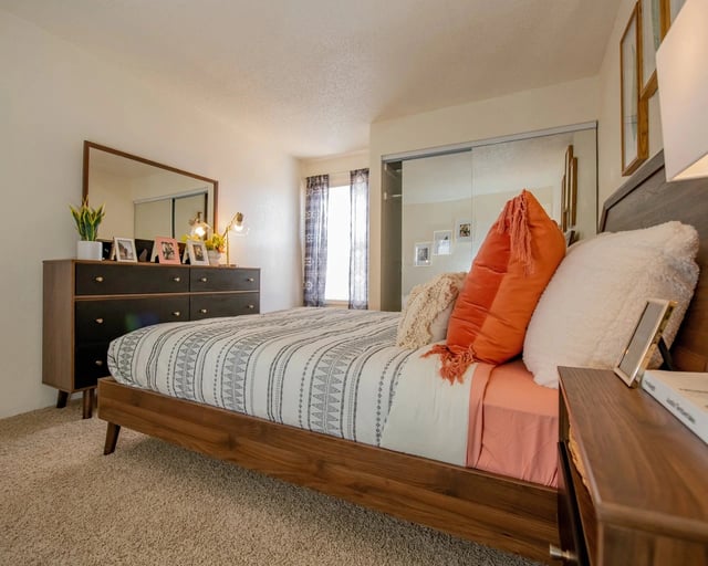 Stylish bedroom with a wooden bed frame, patterned bedding, and a dresser with a mirror.