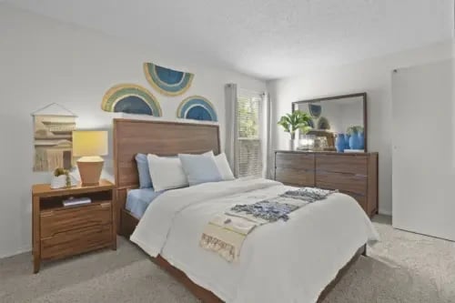 Bedroom with a wooden bed frame, two nightstands, dresser, and window light.