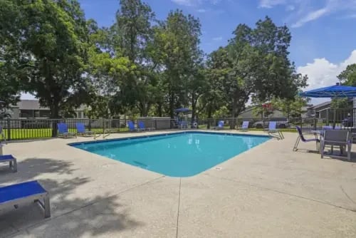Outdoor community pool with lounge chairs and surrounding trees.