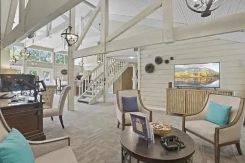 Bright communal lounge with couches, chairs, a staircase, and wall decor.